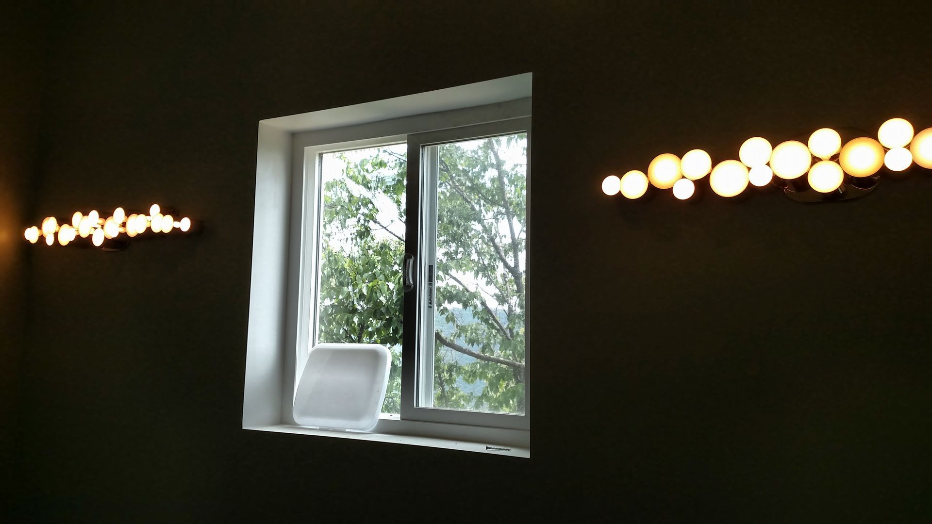 Window between two walls, each with a horizontal light fixture. Open window shows green trees.