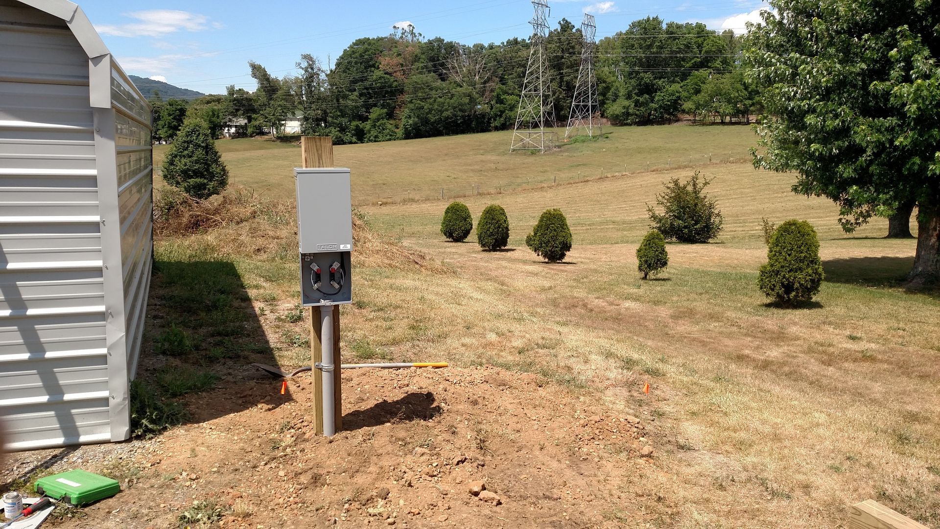 Electrical box on a pole in a yard next to a shed and small trees.