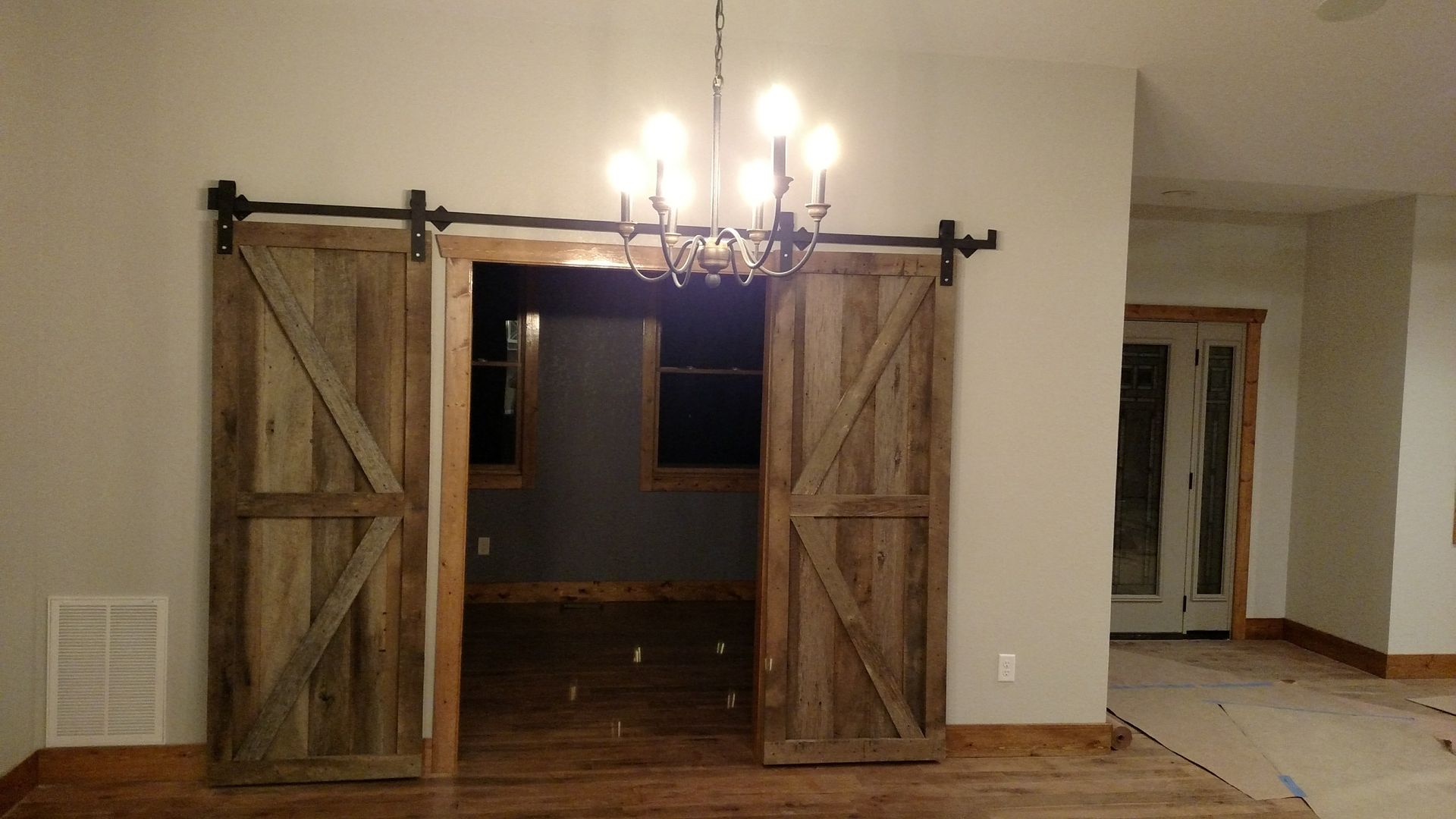 Barn doors open to a dark room, with a chandelier hanging above them.
