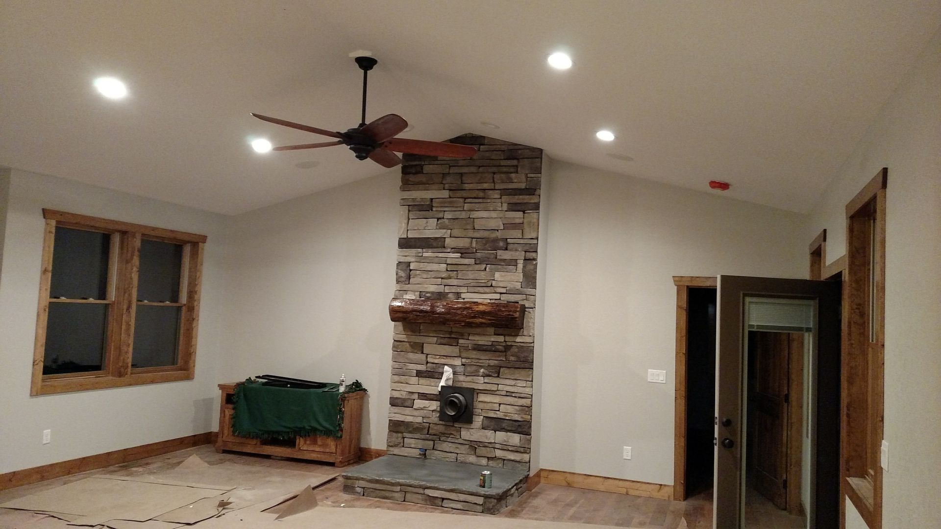 Living room with stone fireplace, wood trim, ceiling fan, recessed lighting, and a partially covered wood chest.