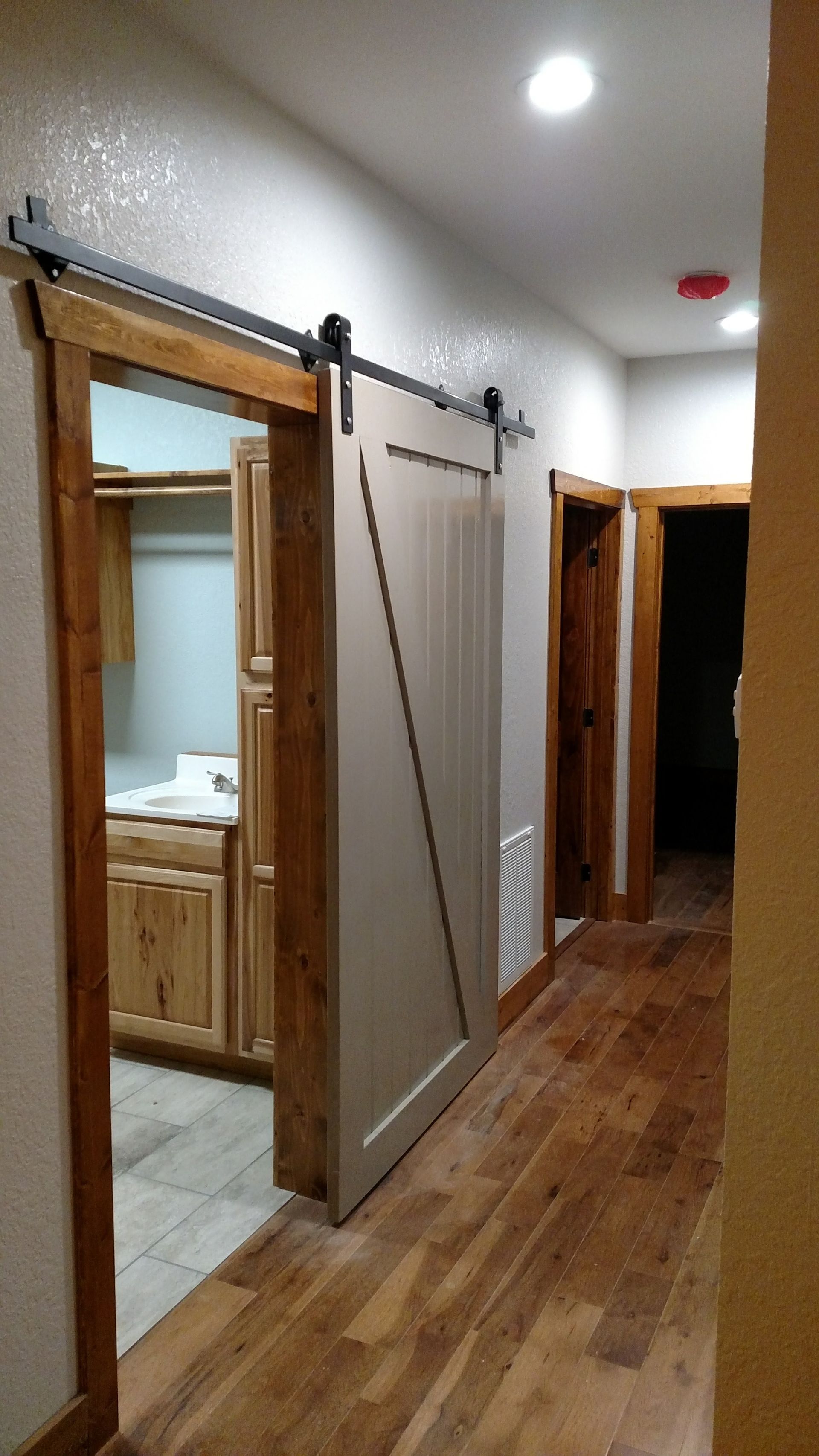 Hallway with a barn door. The door is cream-colored and slides on a black track. The frame and wood floors are light brown.