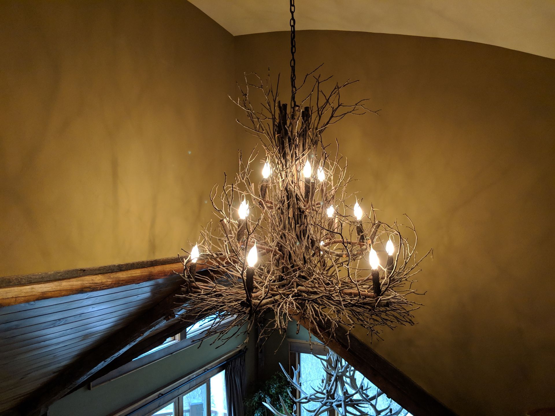 Ornate branch-like chandelier with lit bulbs hangs from a sloped ceiling.