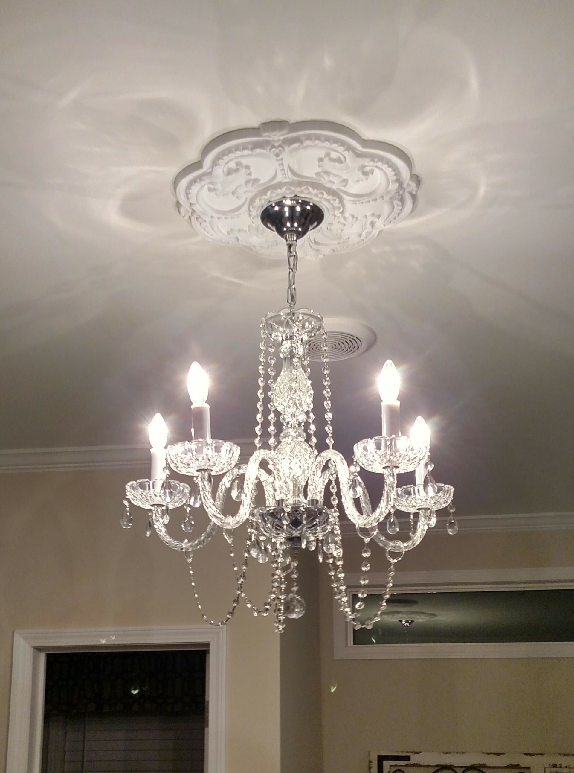Crystal chandelier hanging from a decorative ceiling medallion; lit candles cast shadows.