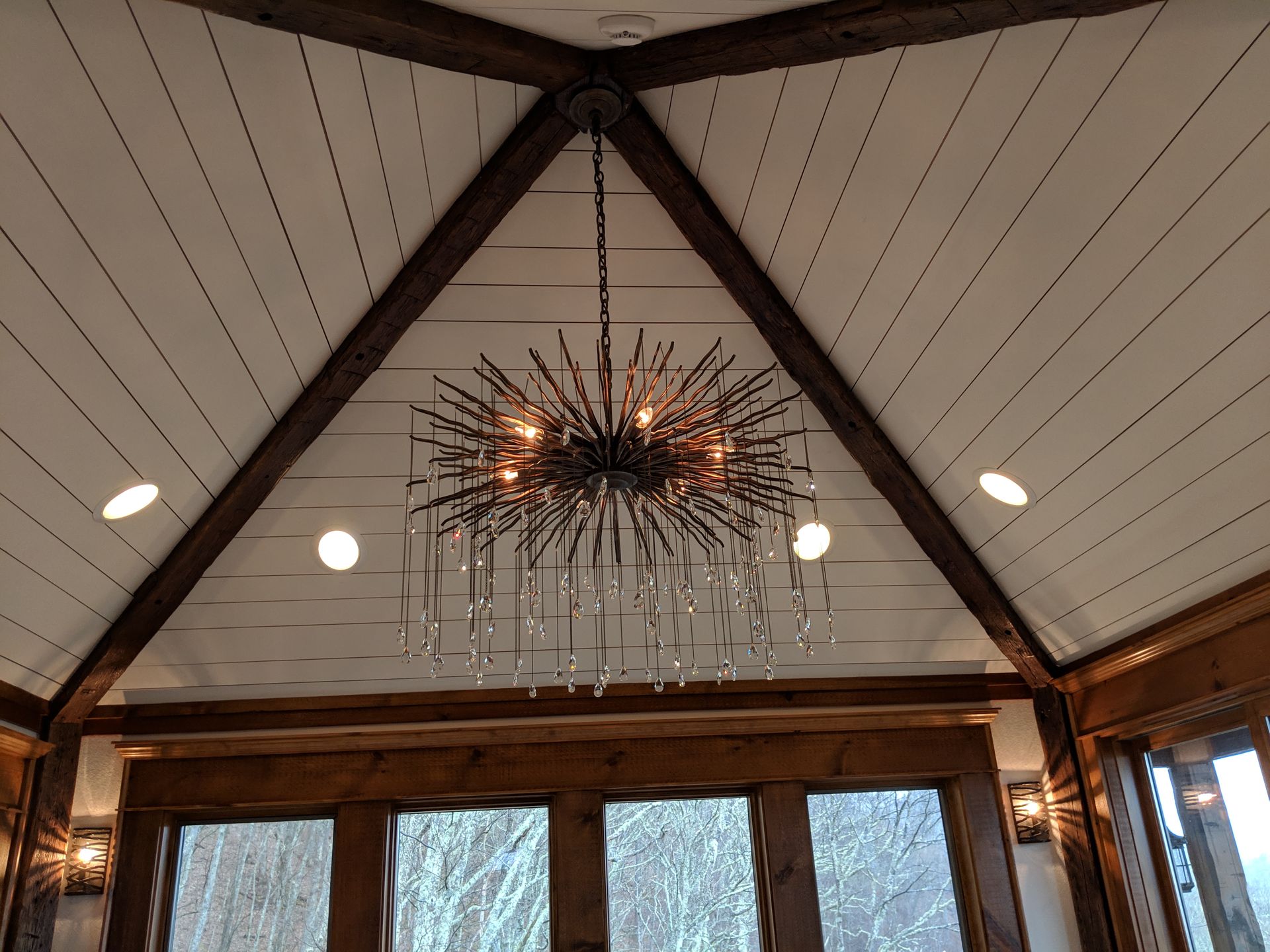 Ornate chandelier hanging in a room with a wood-beamed, white plank ceiling.