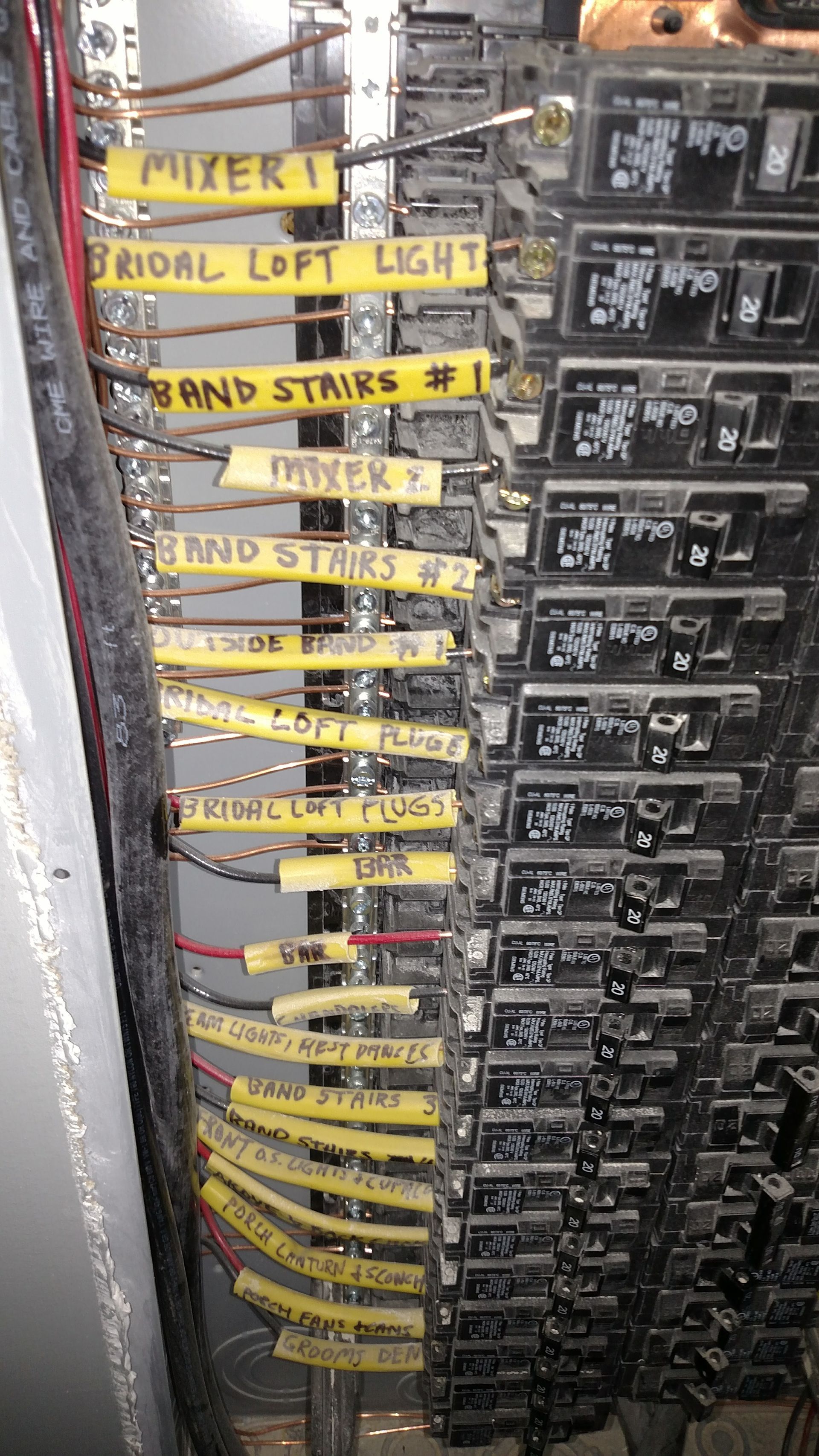 Electrical panel with labeled circuit breakers. Wires and yellow labels.