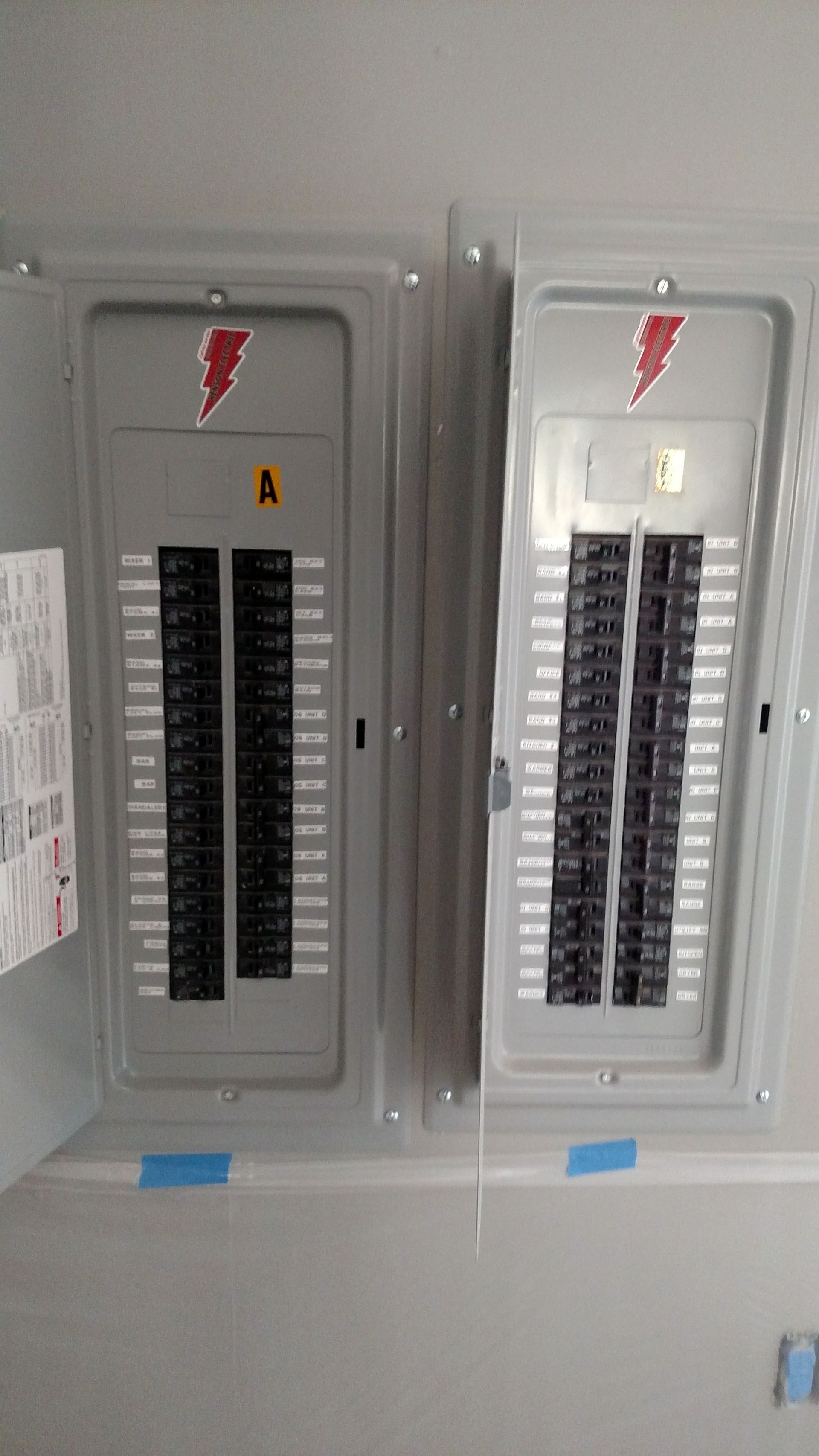 Two open electrical breaker boxes with rows of switches, mounted on a wall.