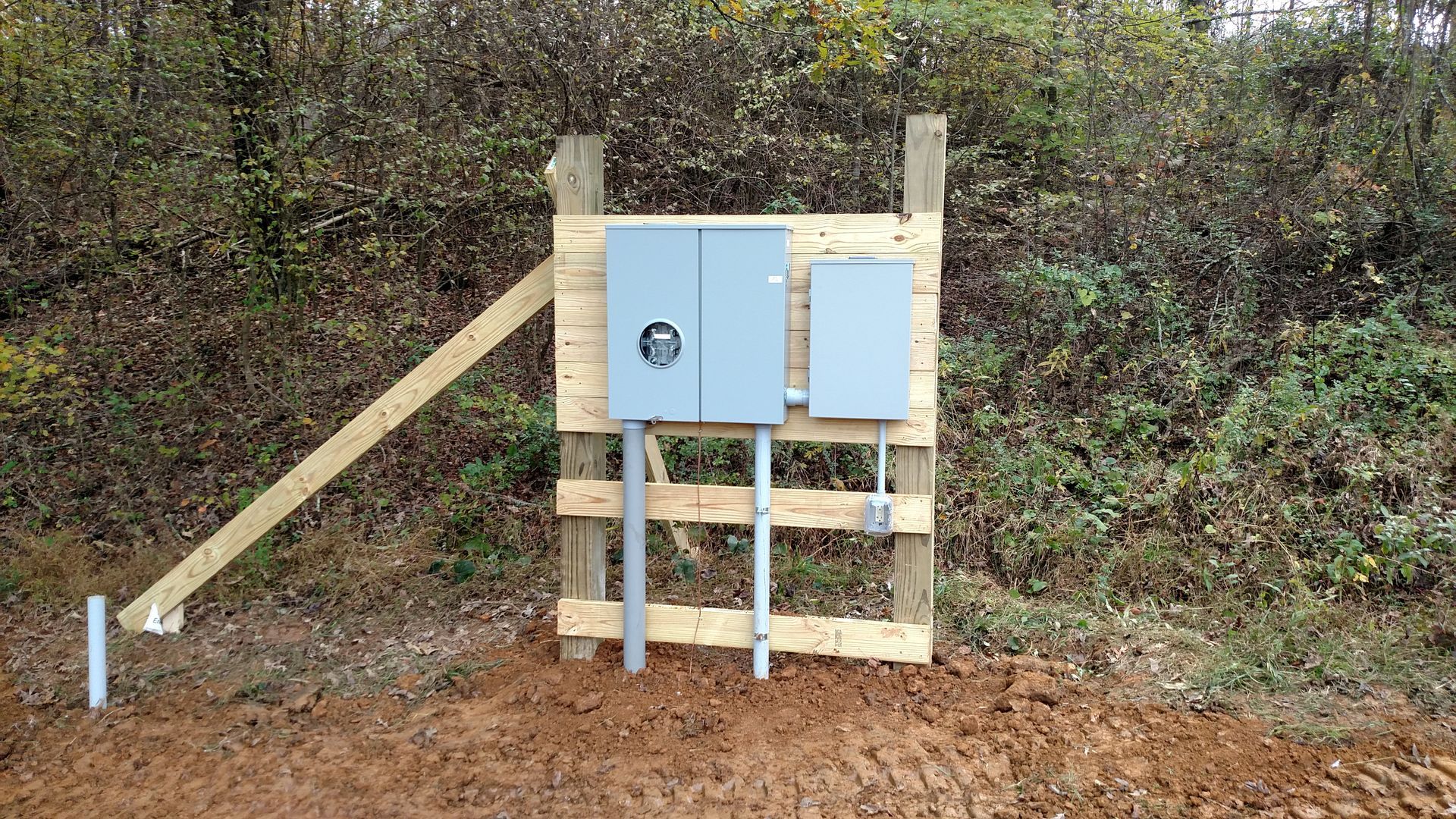 Wooden structure with electrical boxes, conduits, and support beam in a wooded area.