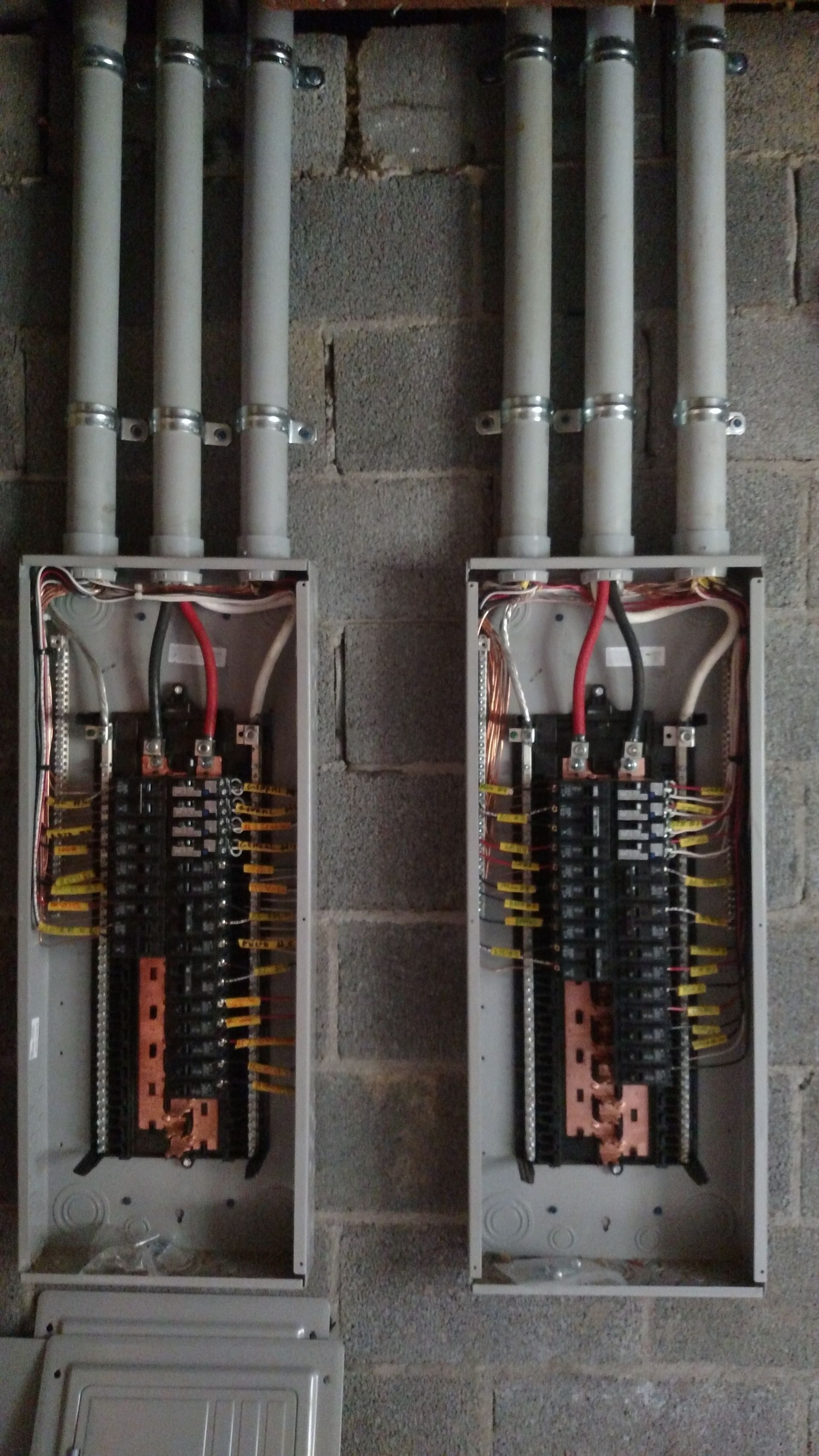 Two gray electrical panels mounted on a brick wall with gray conduit pipes attached. Wires are visible inside the panels.