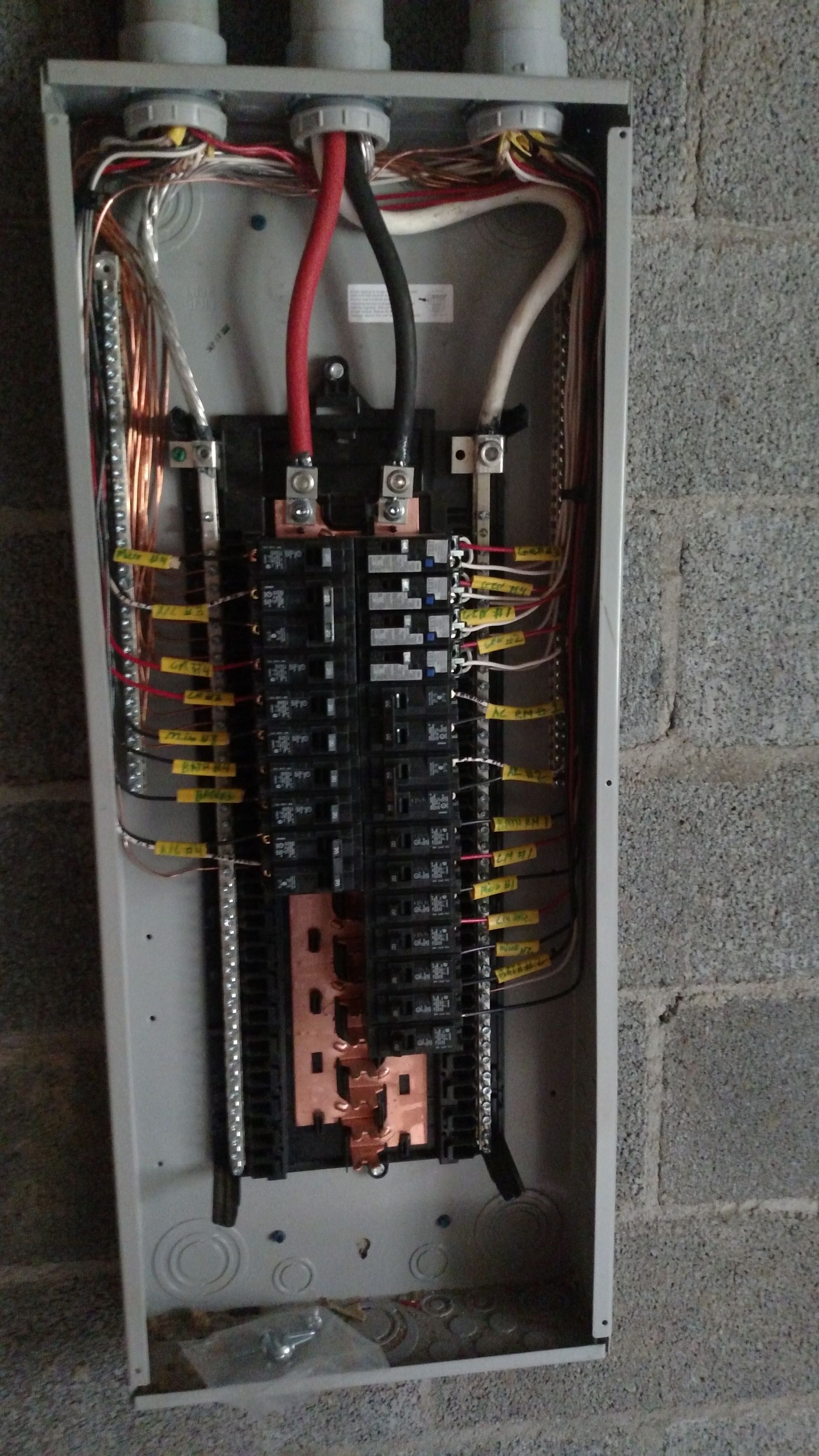 Electrical panel with wires and breakers installed on a gray block wall.