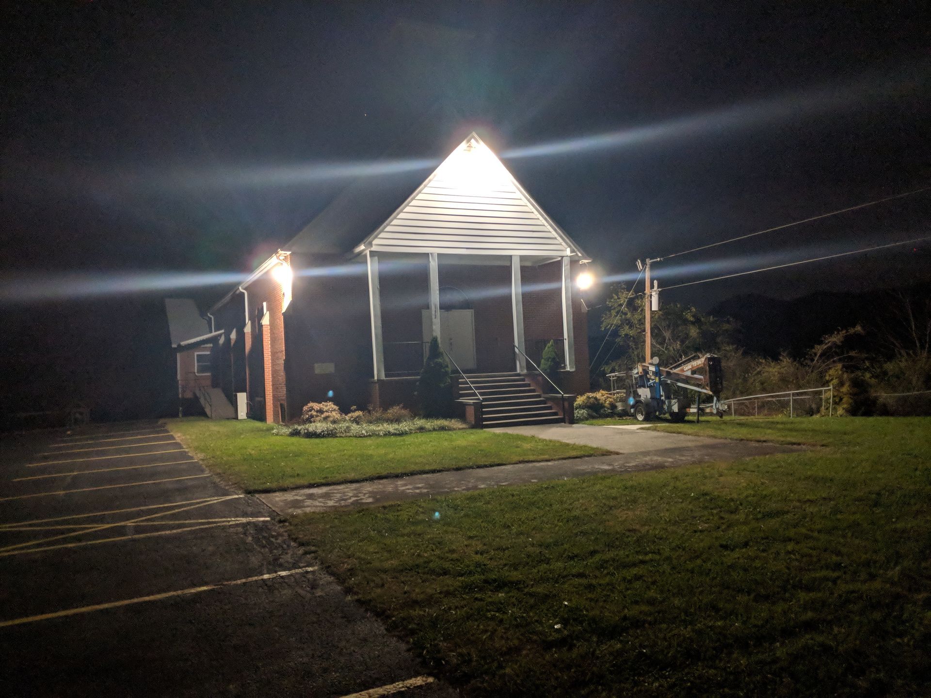 A small brick building, lit up at night, with a porch and steps, and a small lawn.