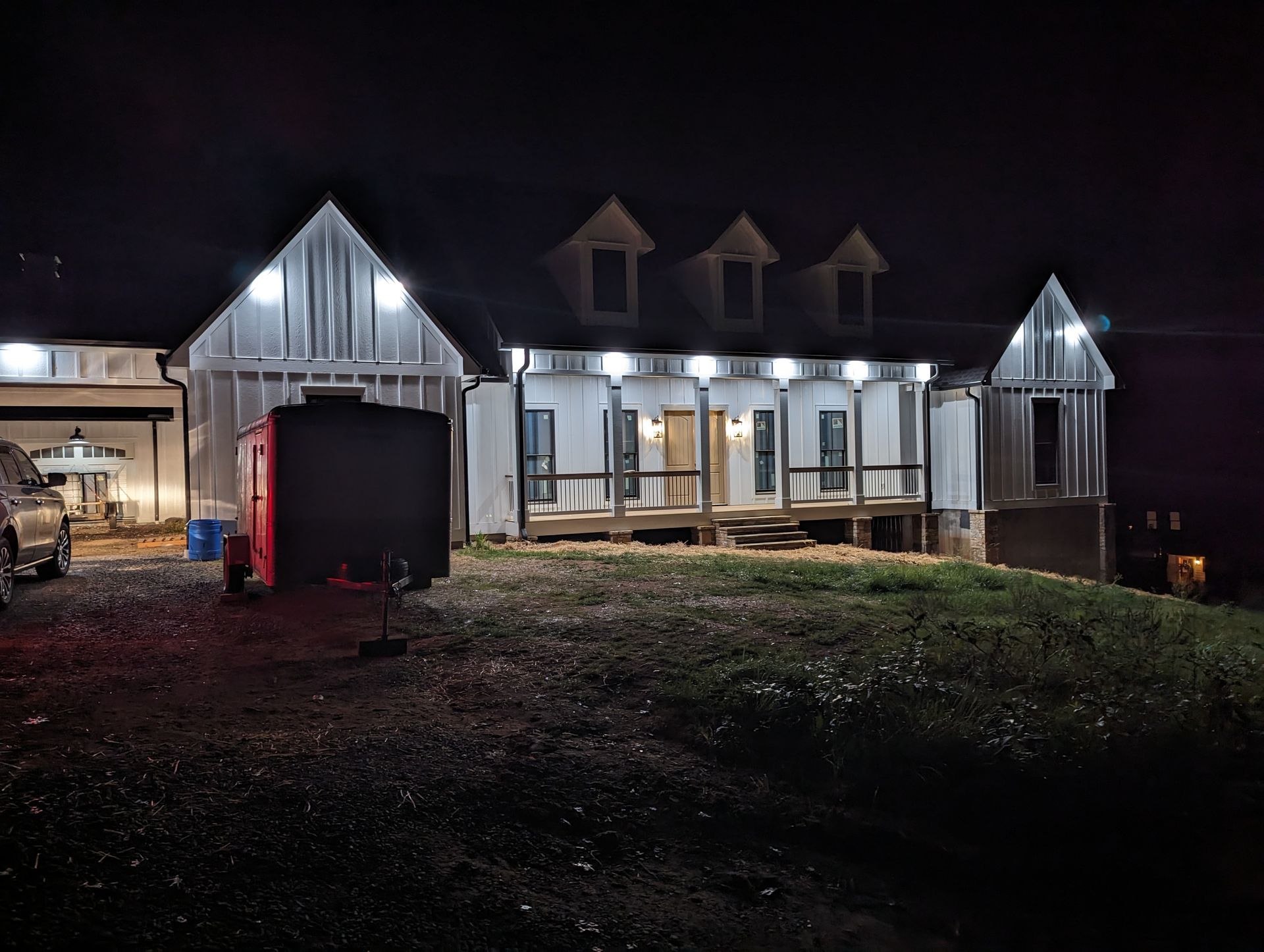 Night view of a white house with bright lights. A red container sits in front.