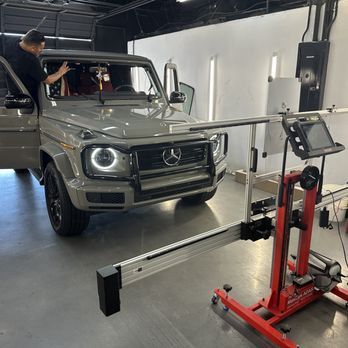 A person working on a gray Mercedes-Benz SUV in a repair shop. Alignment tool in foreground.