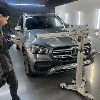 Person using a tablet near a silver Mercedes SUV in a workshop, alignment equipment in front.