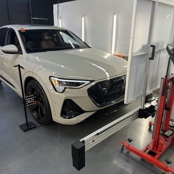 White Audi SUV undergoing alignment in a shop; a calibration device is in front of the car.