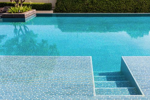 Blue swimming pool with tiled steps and a raised spa edge in sunlight
