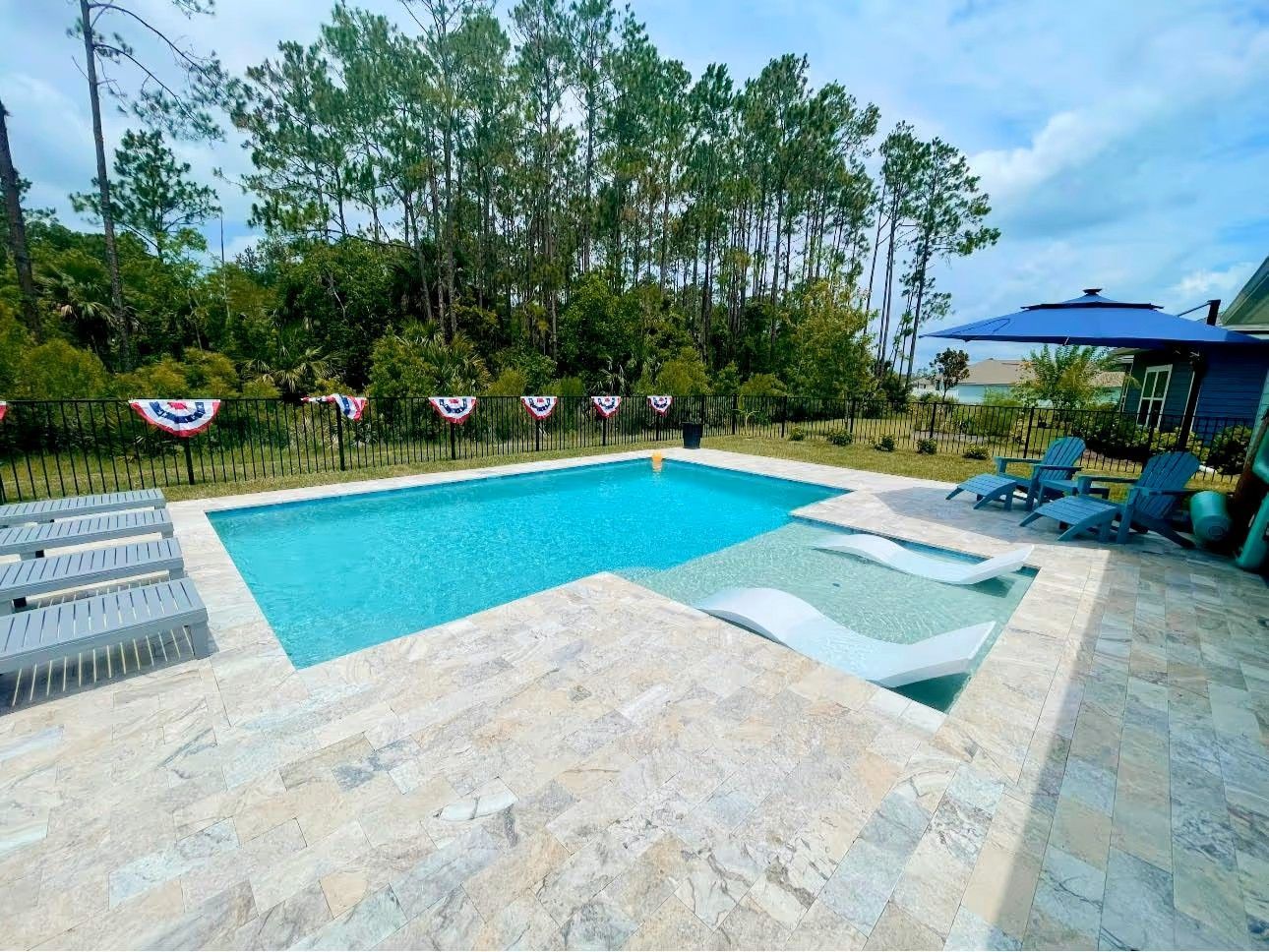 Outdoor pool with turquoise water, lounge chairs, and trees along a decorated deck.
