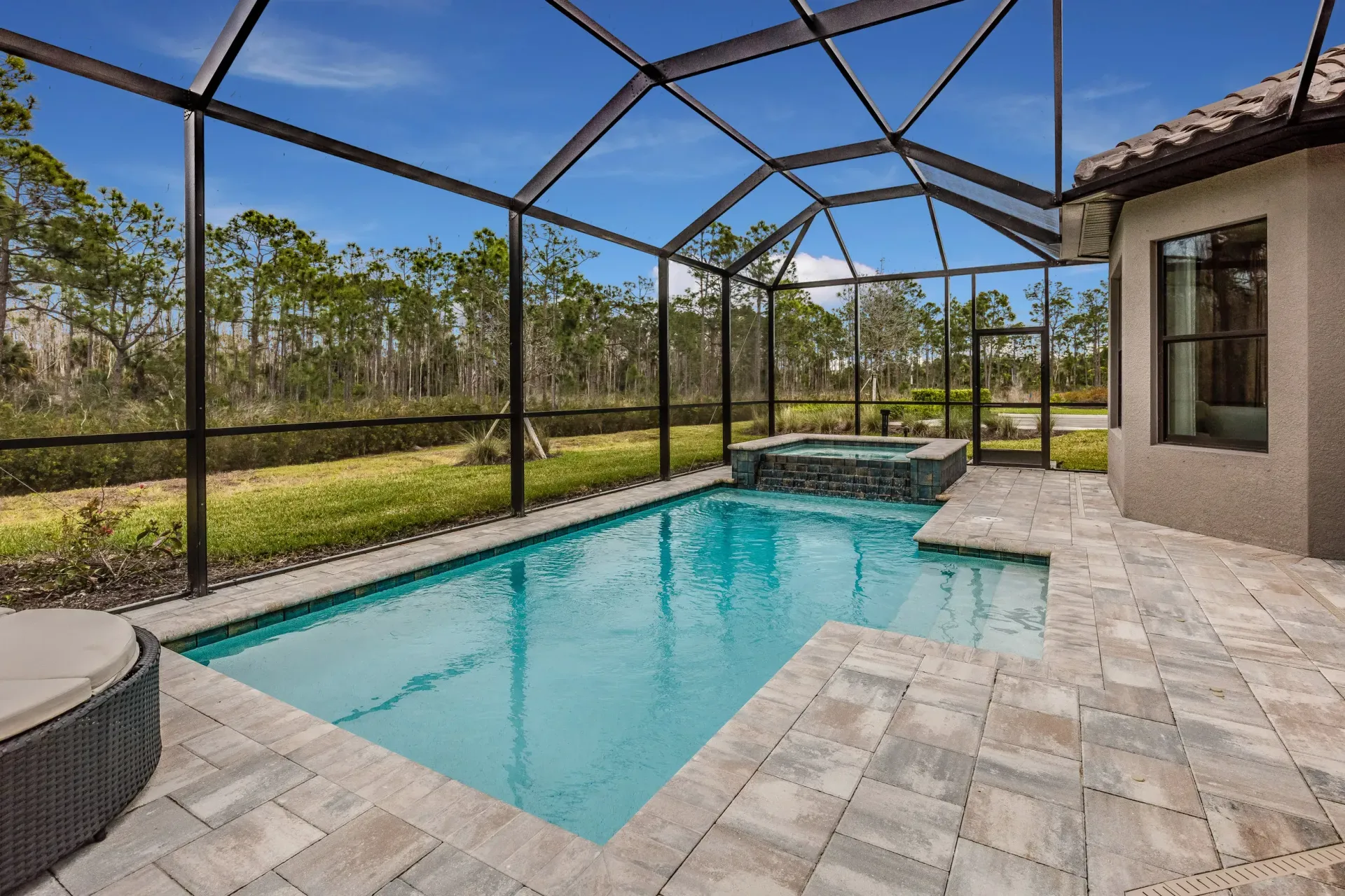 Screened-in backyard pool with turquoise water and stone patio beside a house