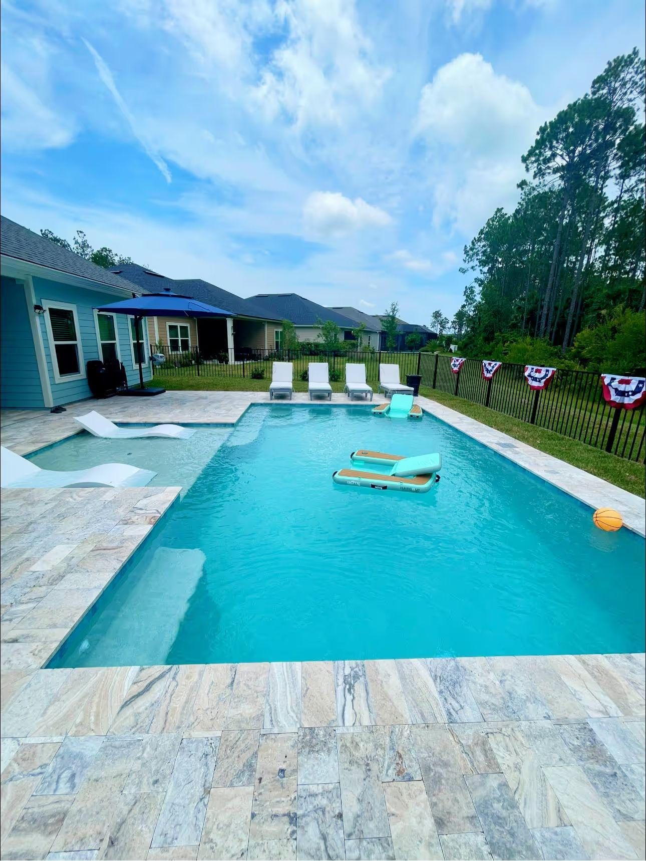 Turquoise backyard pool with lounge chairs, house patio, and mountains under a partly cloudy sky