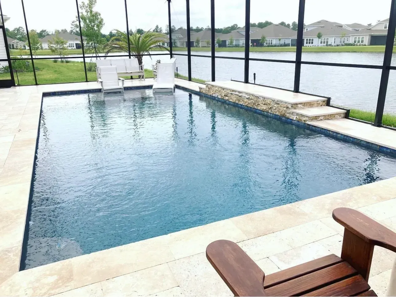 Backyard pool with water, lounge chairs, and a screened-in lanai overlooking a lake.