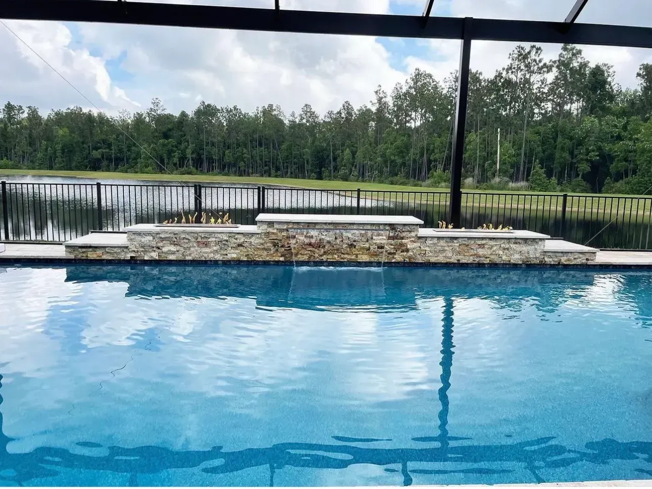 Outdoor pool with blue water, lounge chairs, and a lake and trees in the background.