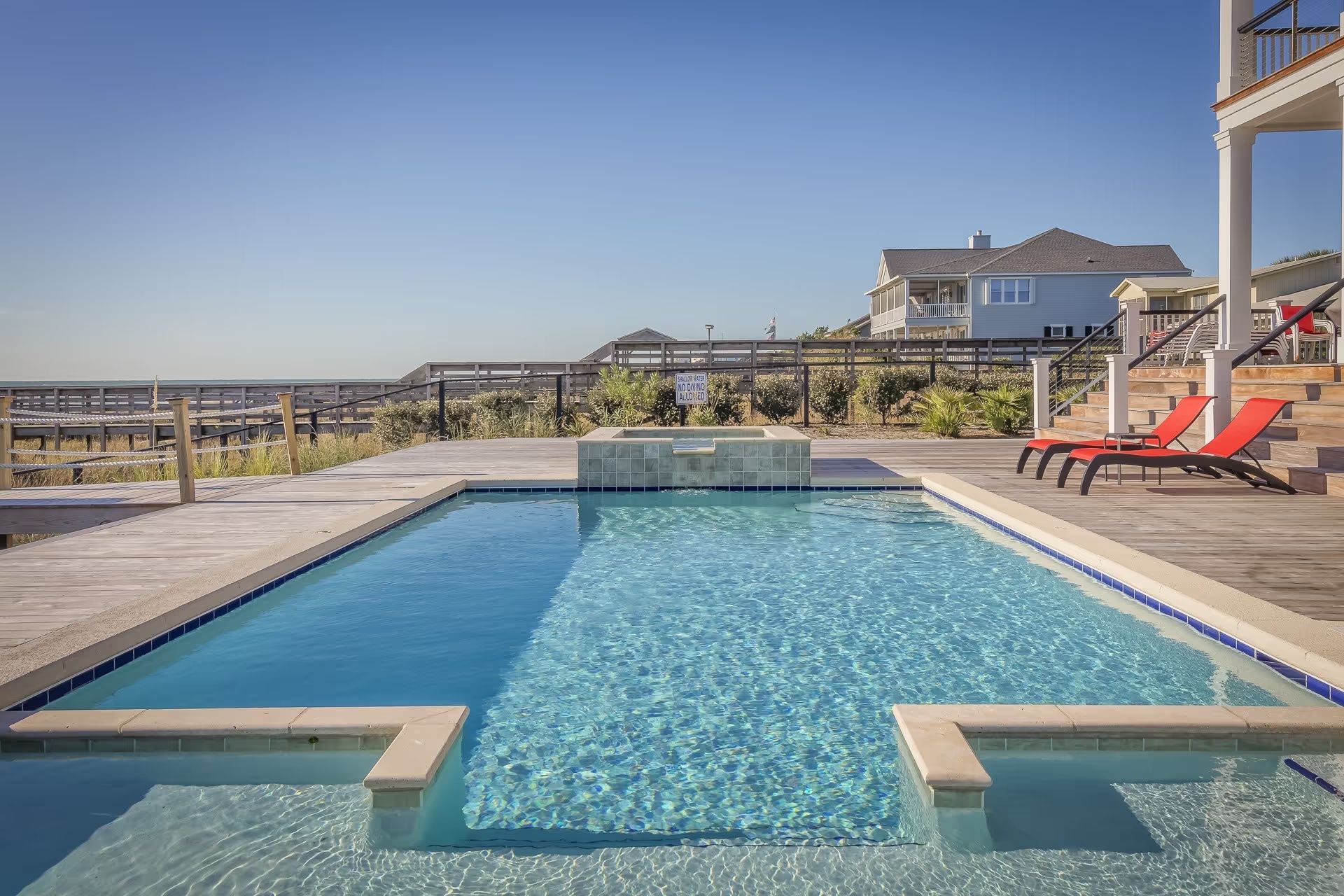 Modern backyard pool with blue water, patio loungers, and a waterfront view under a clear sky