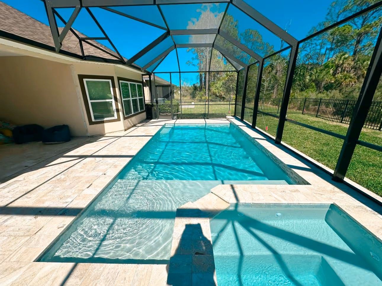 Screened-in backyard pool beside a house, with blue water and a clear sky overhead