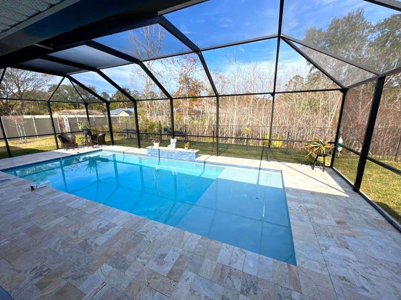 Screened-in backyard pool with blue water and a stone patio under a black metal frame.