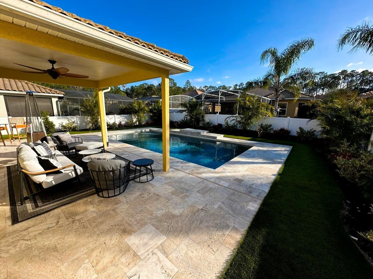 Backyard patio with lounge chairs beside a swimming pool under a covered pergola, sunny day