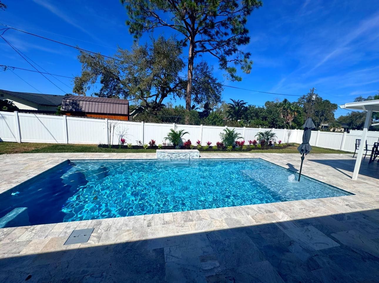 Backyard swimming pool with blue water, white fence, and potted plants under a sunny sky