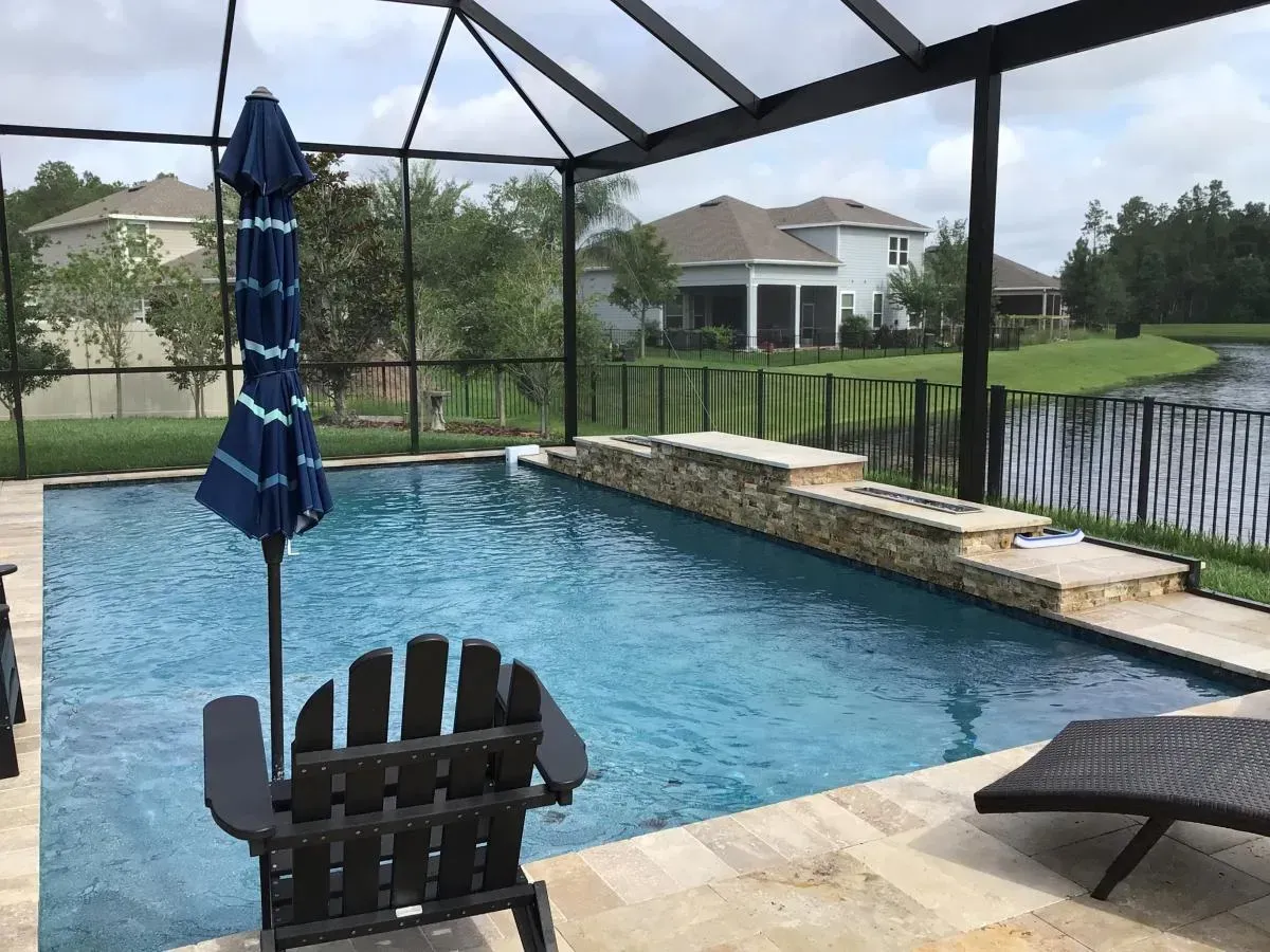 Backyard pool with screened enclosure, blue umbrella, and lounge chair overlooking a lake
