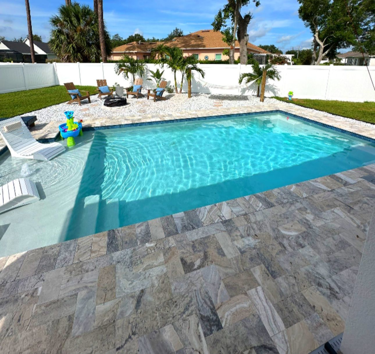 Backyard swimming pool with turquoise water, stone patio, and lounge chairs under a sunny sky