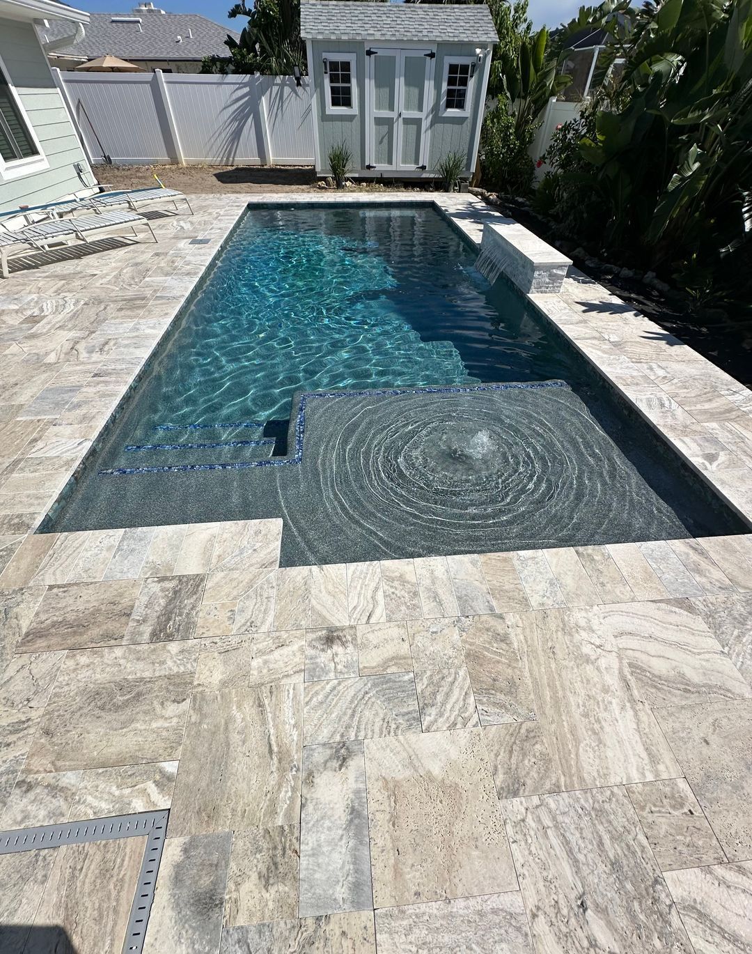 Backyard pool with turquoise water and stone patio, featuring a raised spa at the far end.