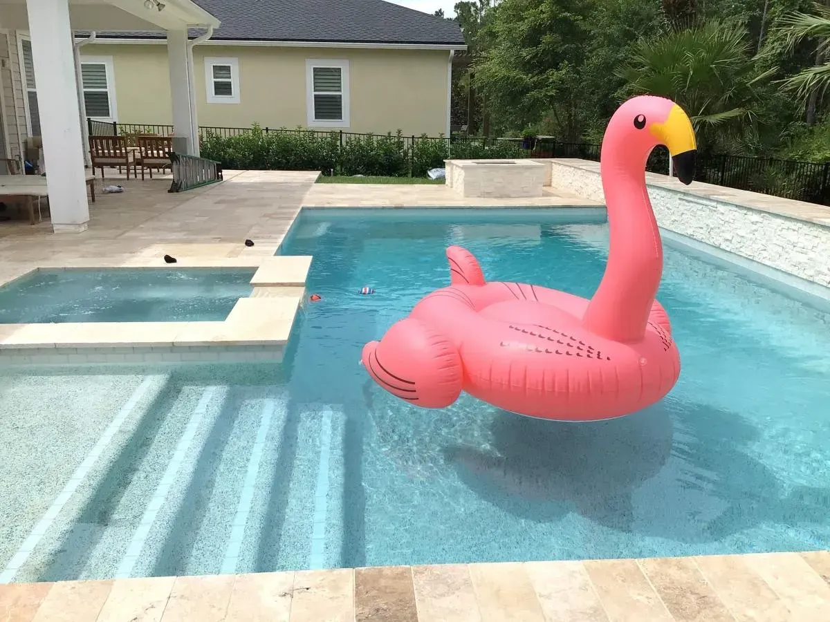 Pink inflatable flamingo float in a backyard swimming pool, with a house and patio in the background