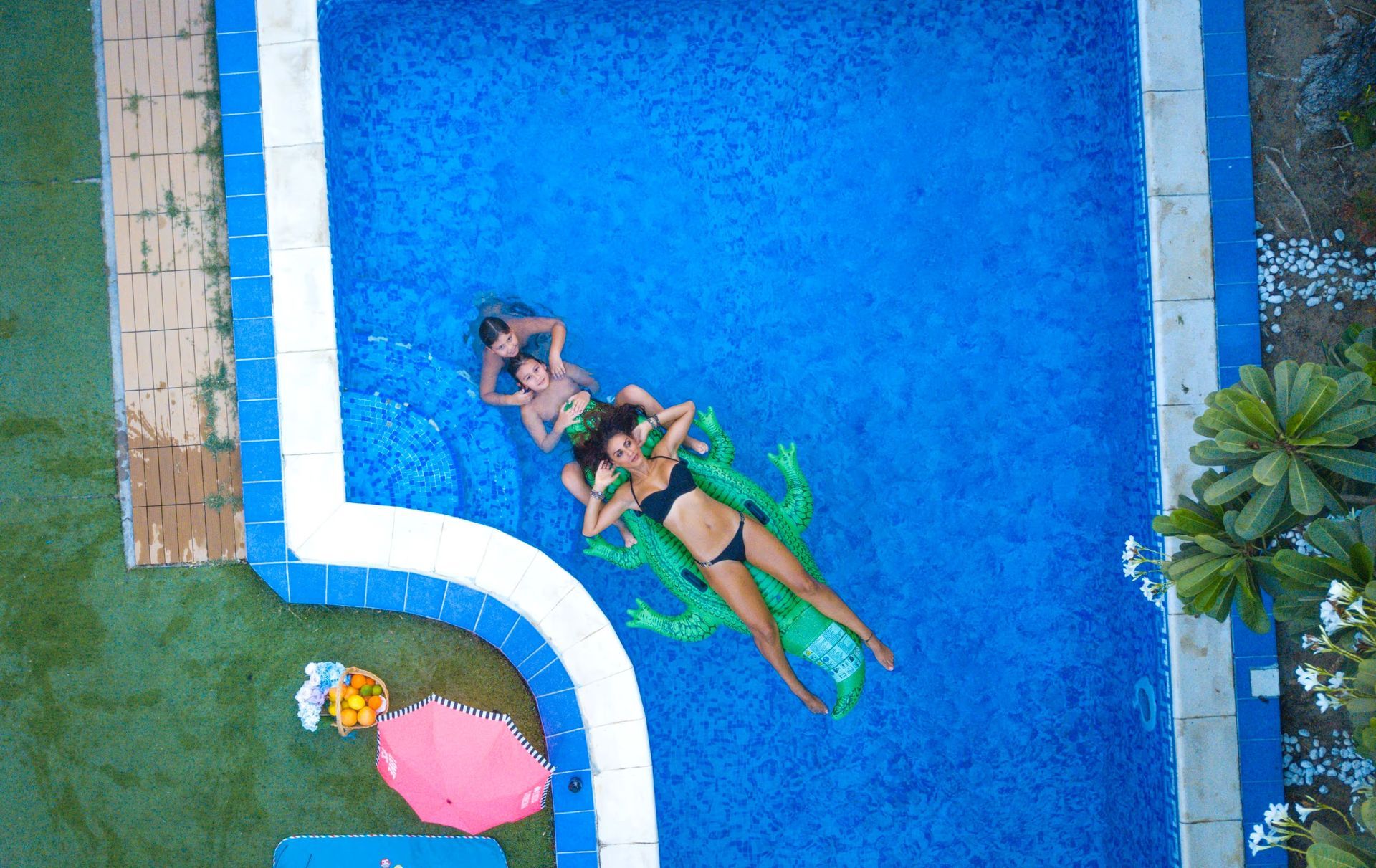 Two people floating on a blue pool beside a curved white edge, with a pink float nearby.