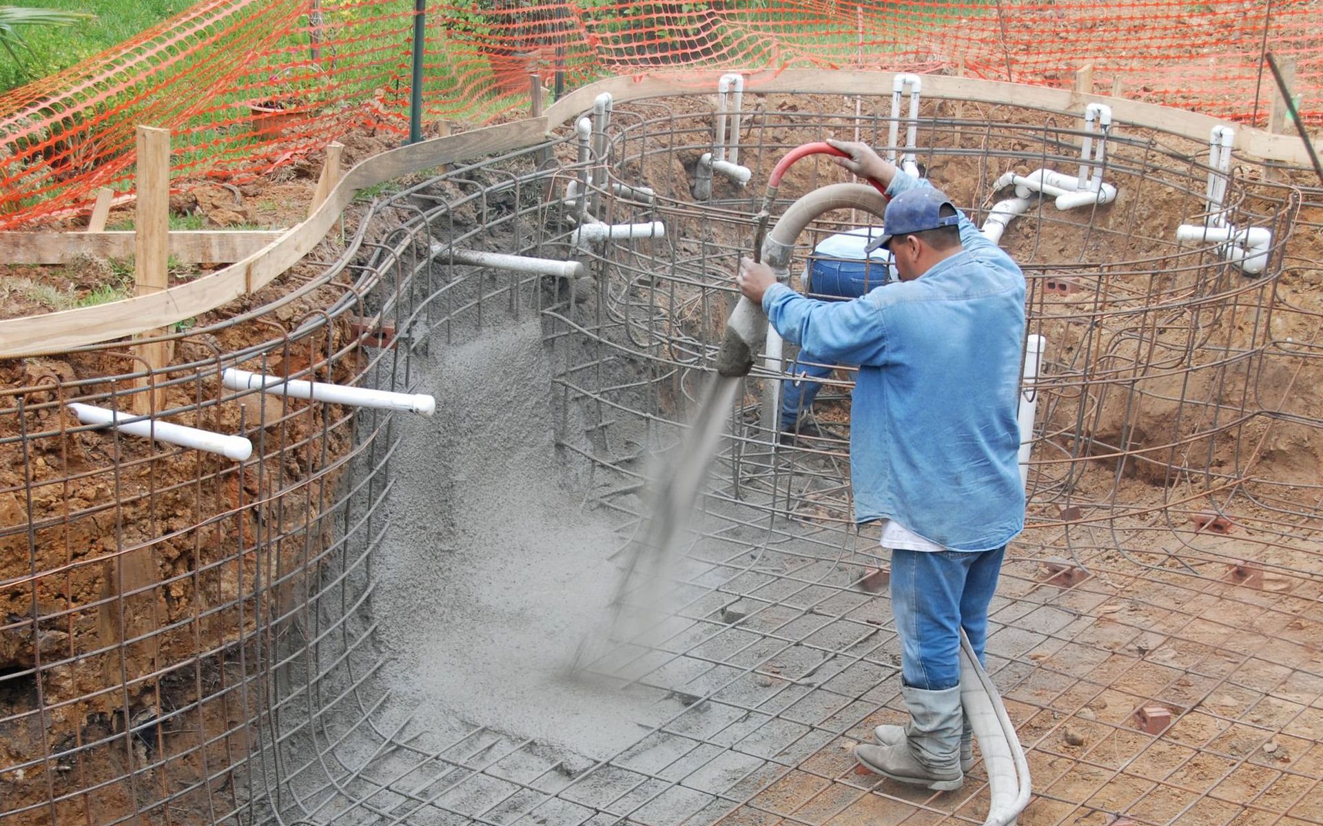 Worker spraying concrete into a rebar foundation pit on a construction site