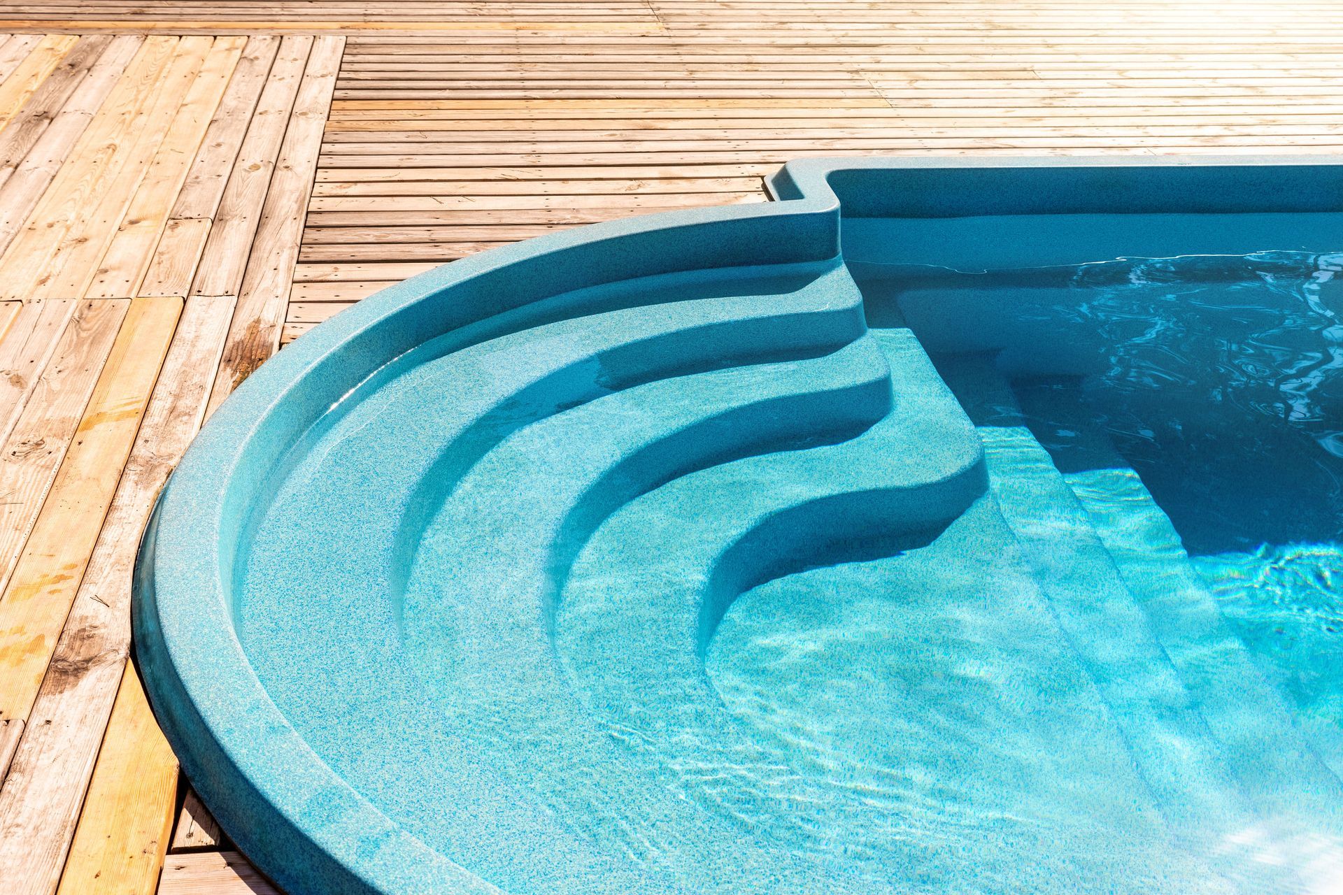 Blue swimming pool with curved entry steps beside a wooden deck