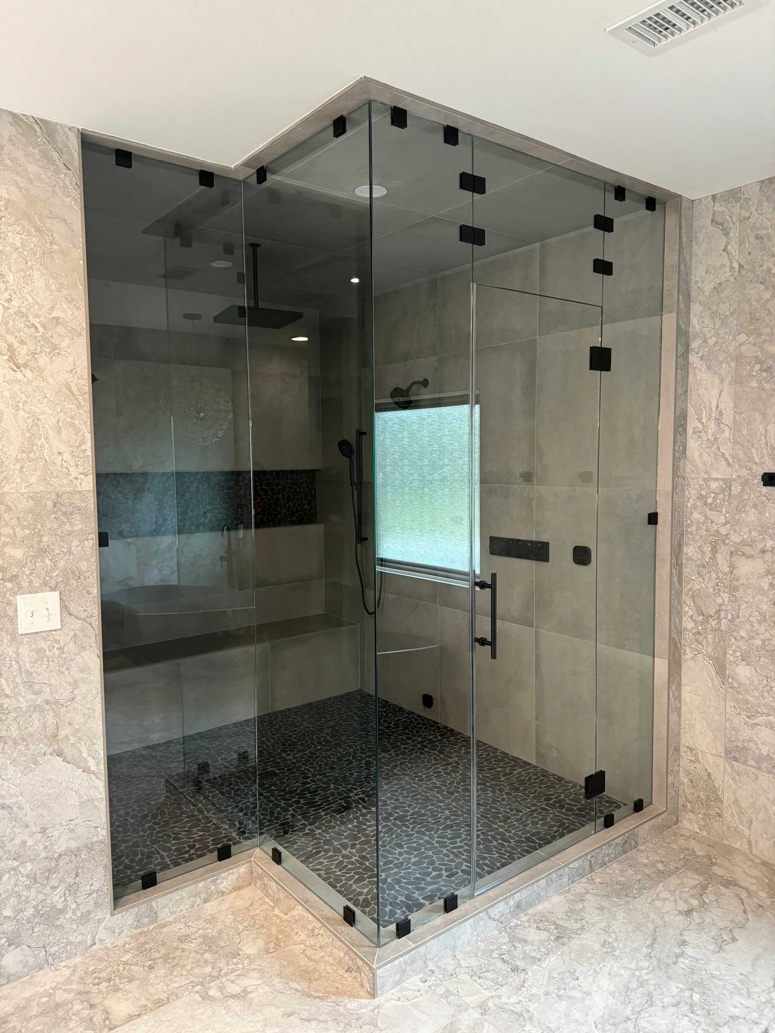A bathroom with a glass shower stall and a window.