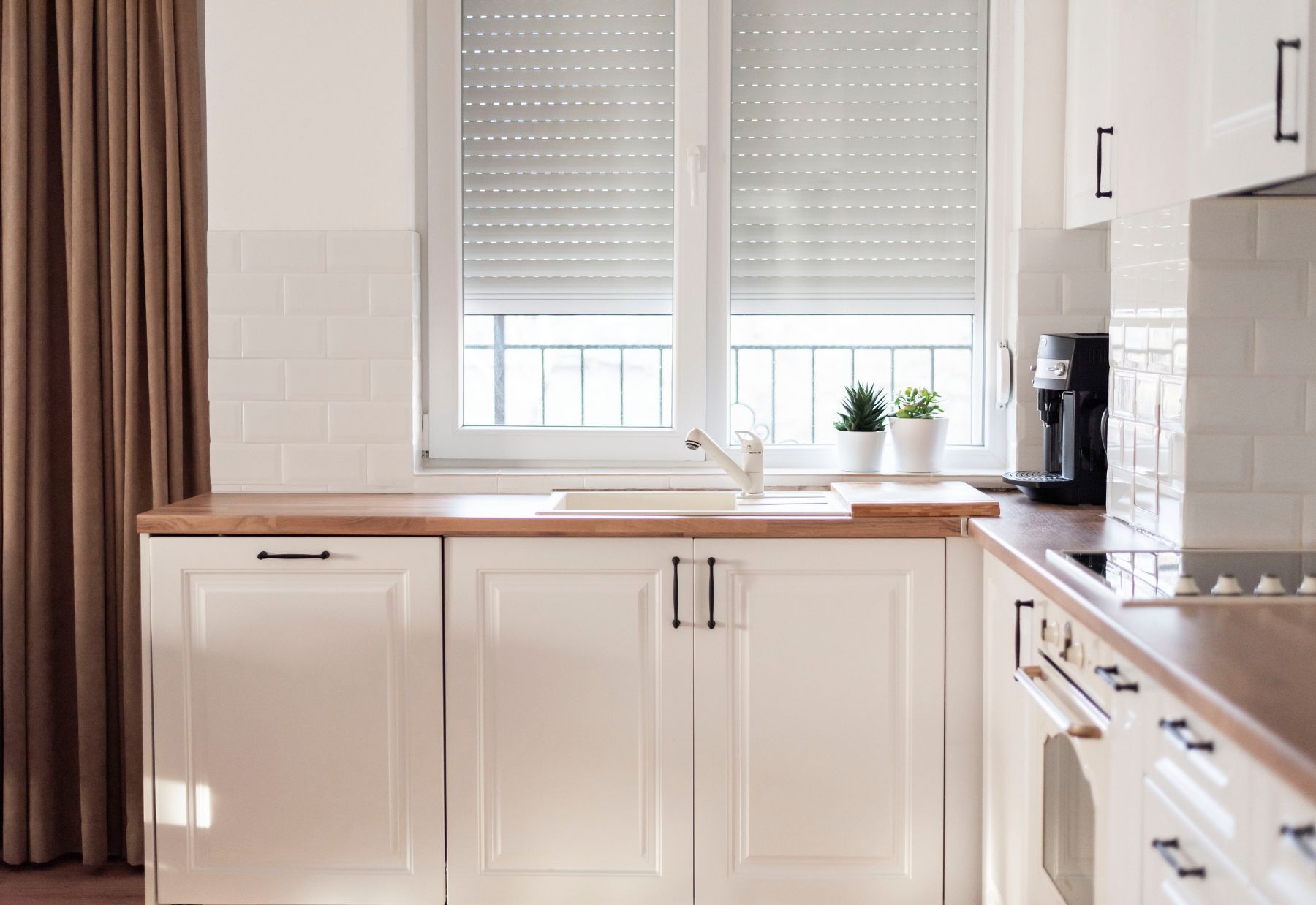 A kitchen with white cabinets , a sink , a stove , and a window.