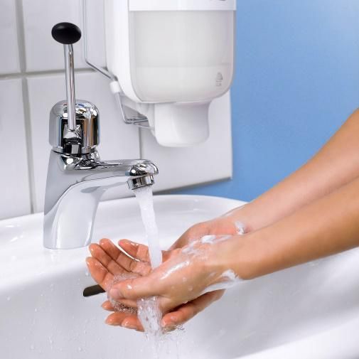 A person is washing their hands in a sink under a soap dispenser.