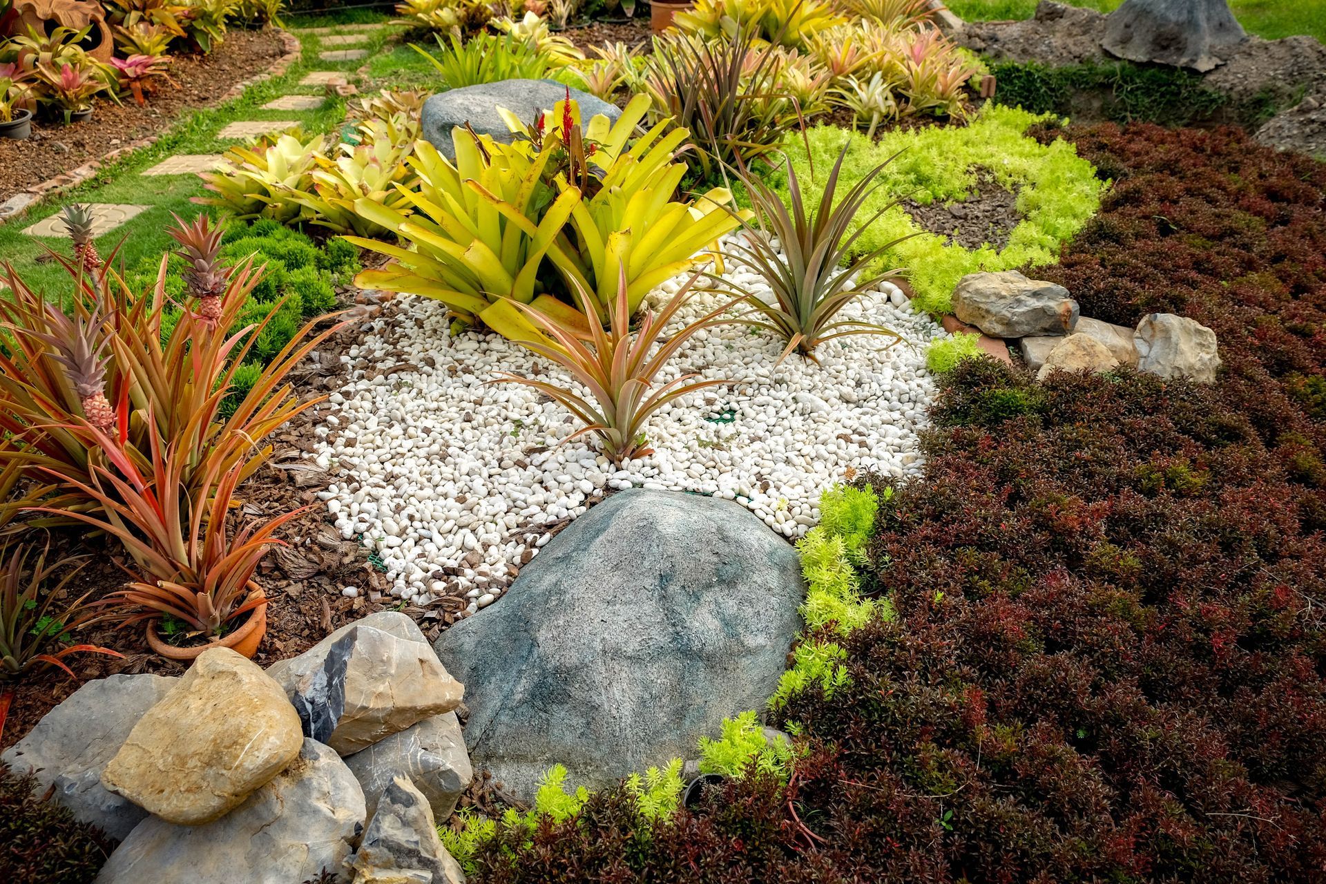 Colorful landscaped garden with varied foliage, white gravel, and large rocks.