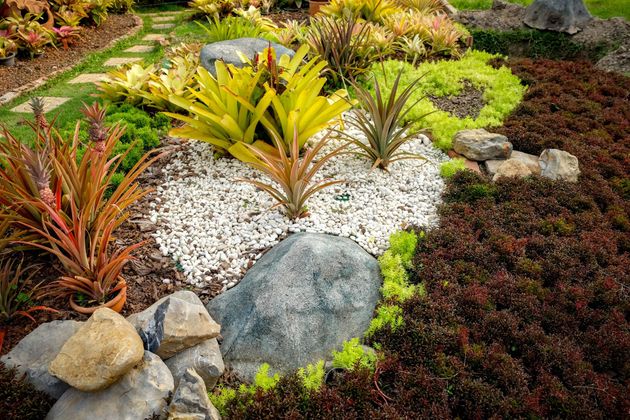 Colorful landscaped garden with varied foliage, white gravel, and large rocks.