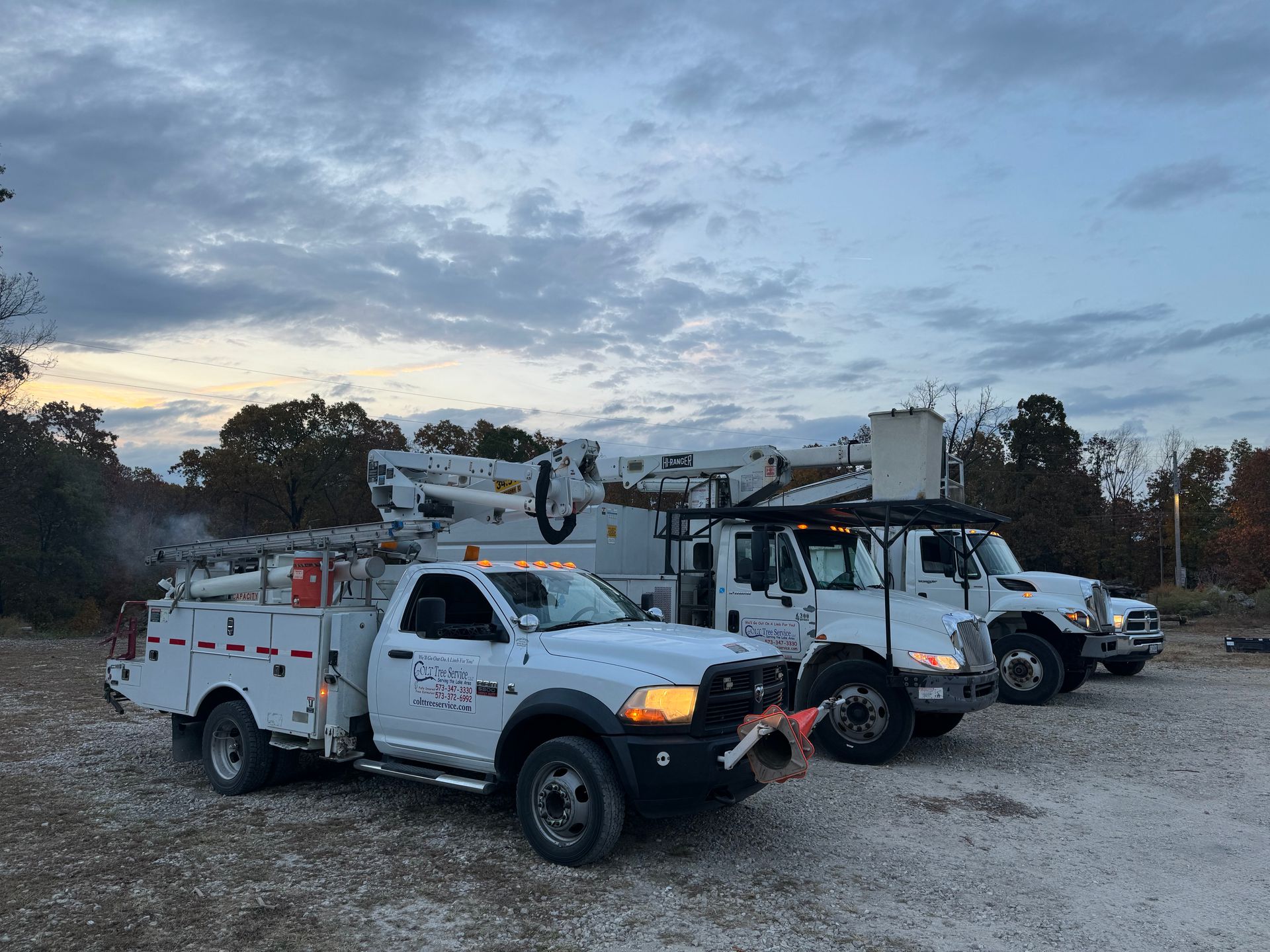 two utility trucks are parked next to each other in a gravel lot.