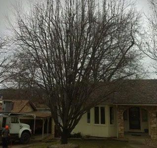 A white truck is parked in front of a house with a tree in front of it.