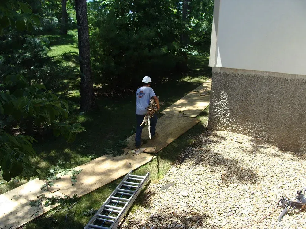 A man wearing a hard hat is walking across a wooden walkway next to a ladder.