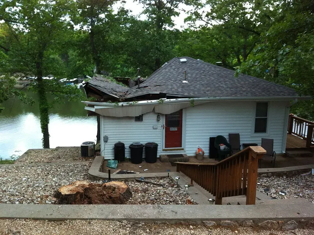 A white house with a red door sits next to a body of water.