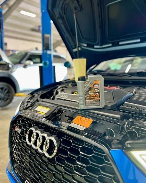 Blue Audi with hood open in a garage, oil and funnel on the engine, ready for maintenance.
