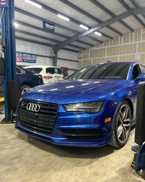 Blue Audi sports car in a garage with a car lift, other vehicles visible in the background.