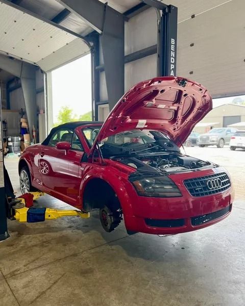 Red Audi TT convertible on a lift in a garage with the hood open, revealing the engine.