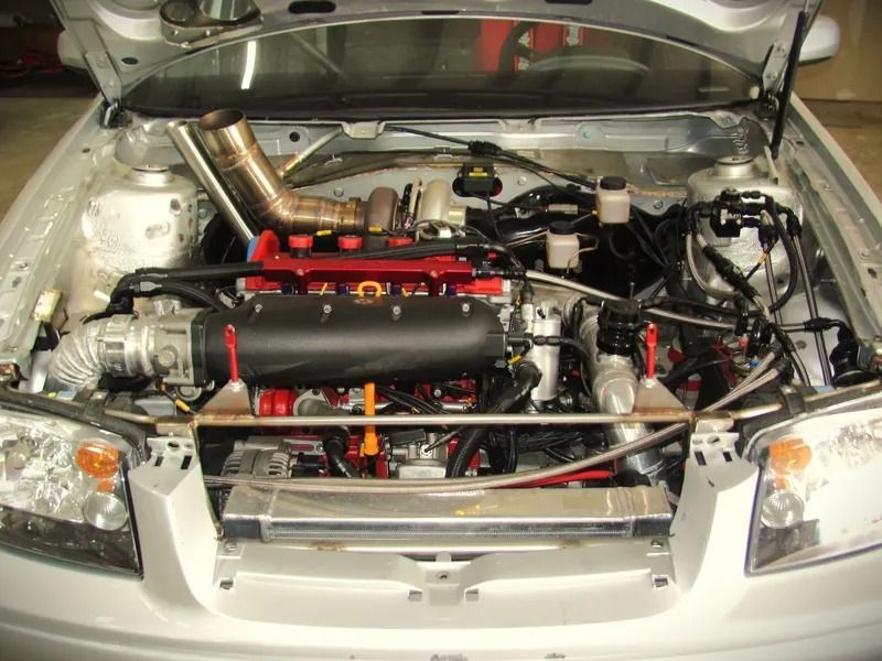 Silver car engine bay, modified with red and black components, large intake, and custom exhaust piping.
