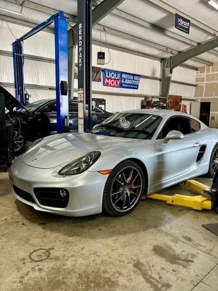 Silver Porsche Cayman sports car on a lift in a repair shop.